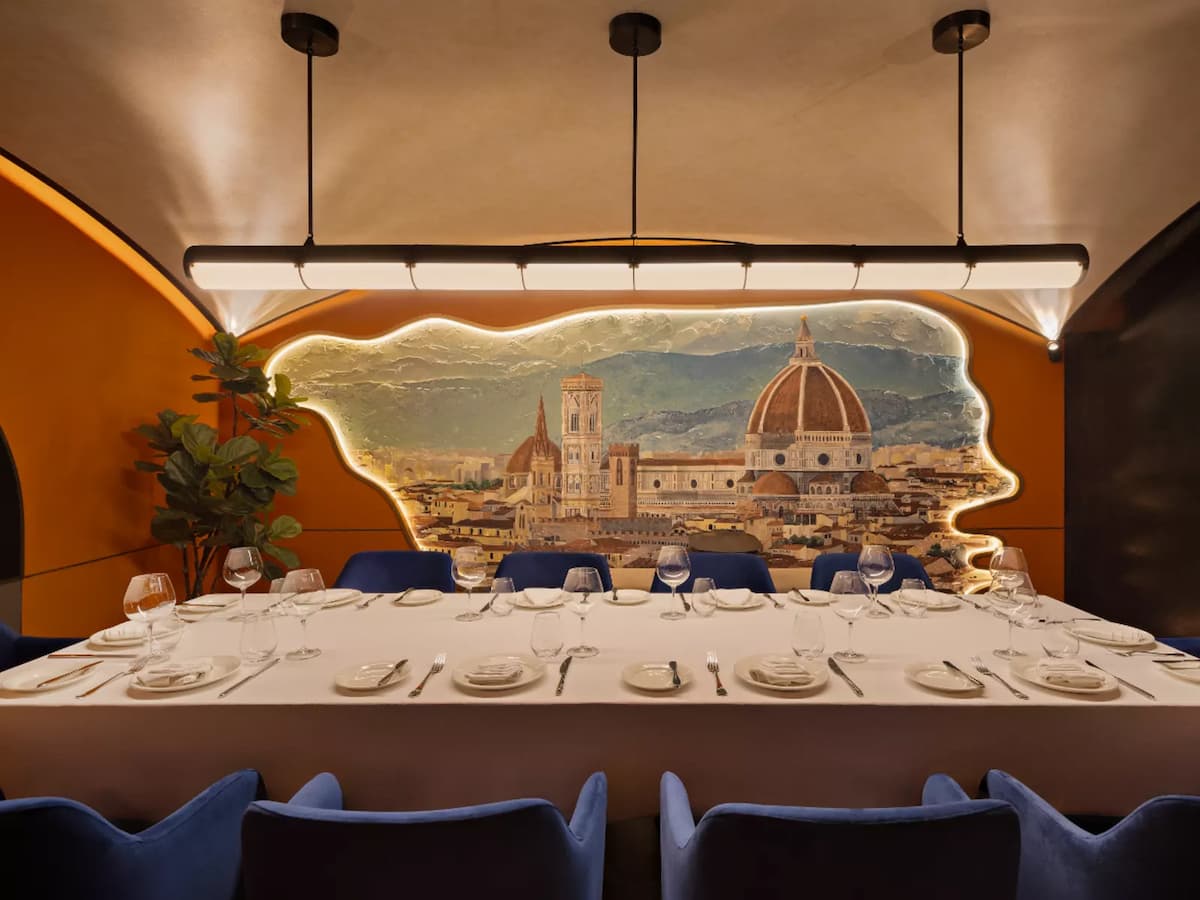 Elegant private dining room with long set table, blue chairs, and mural backdrop of a historic city skyline.