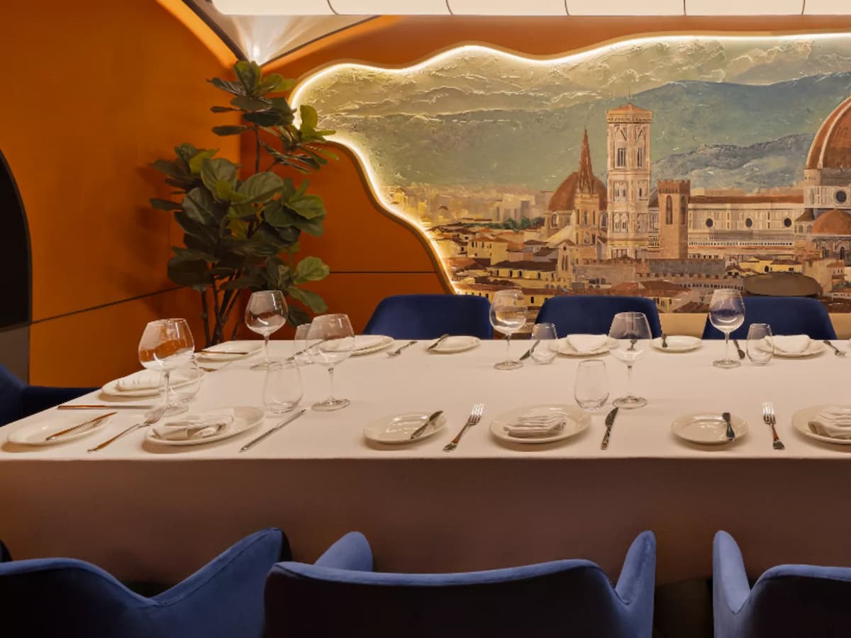Elegant private dining room with long set table, blue chairs, and mural backdrop of a historic city skyline.