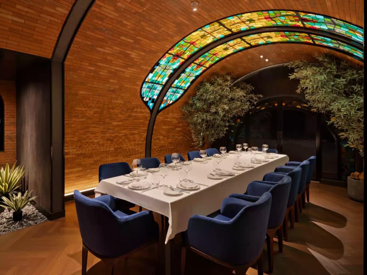 Private dining room with long set table, blue upholstered chairs, and stained glass arched ceiling.