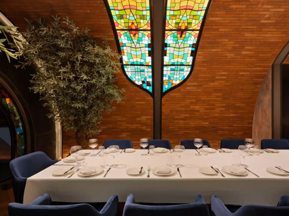 Private dining room with long set table, blue upholstered chairs, and stained glass arched ceiling.