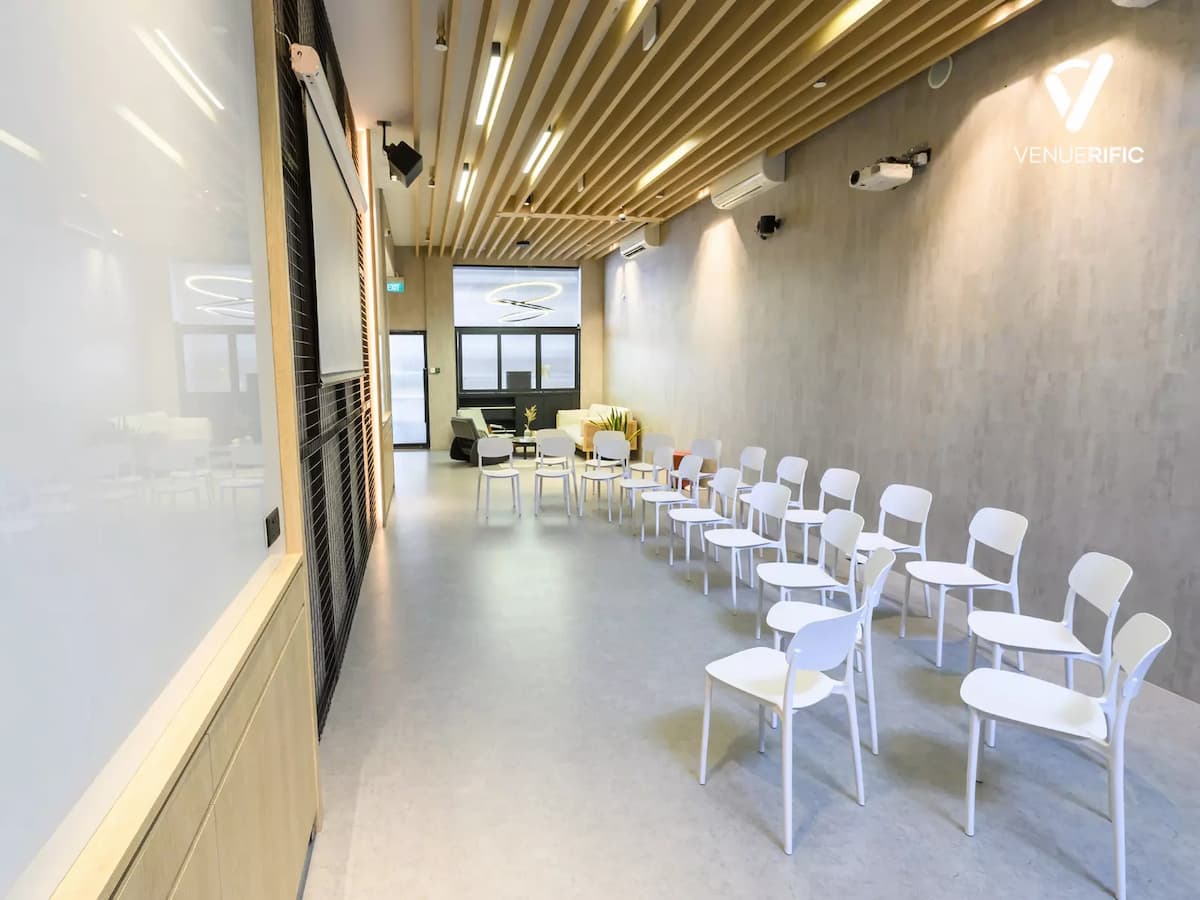 Bright presentation room with white chairs, wood slat ceiling, projector setup, and a modern minimalist design.