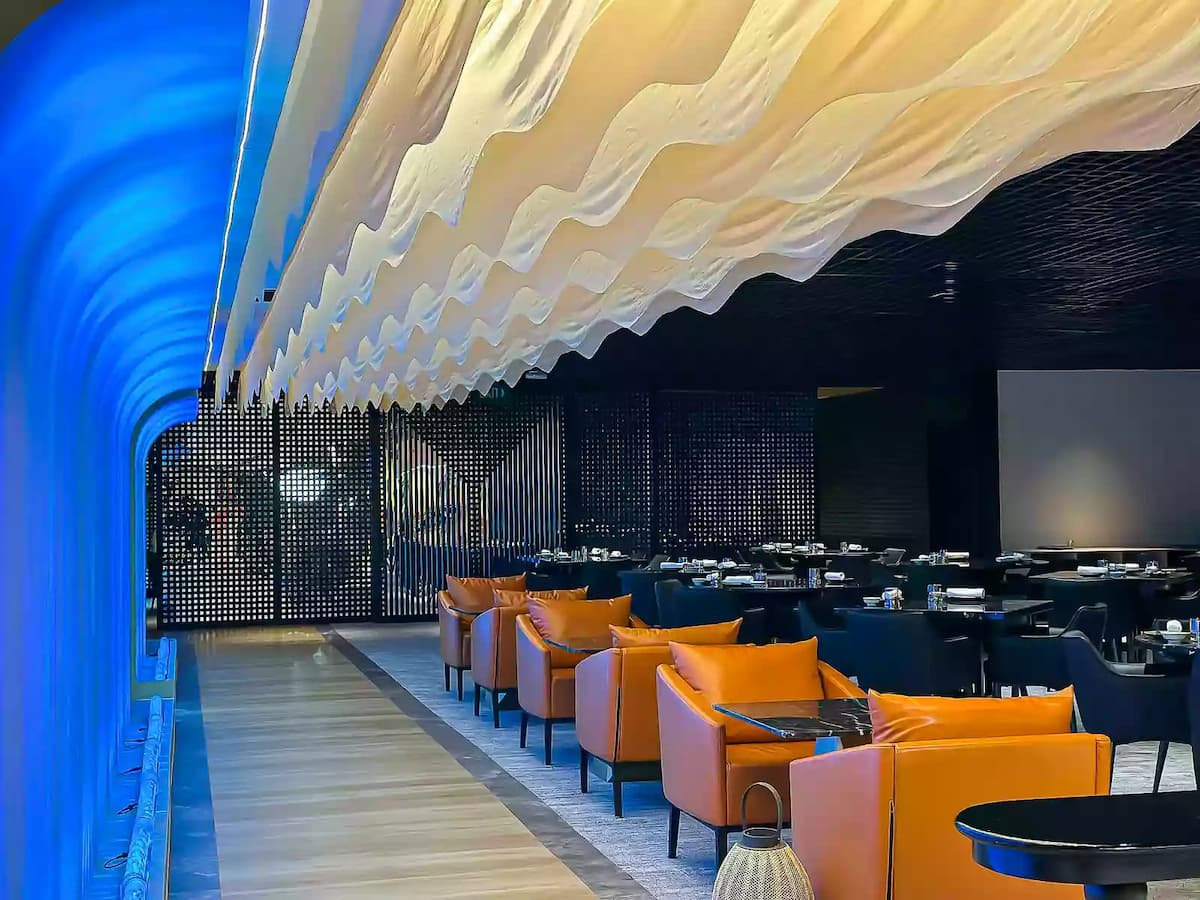 Contemporary dining venue with wave ceiling, lounge seating, and modern lighting.