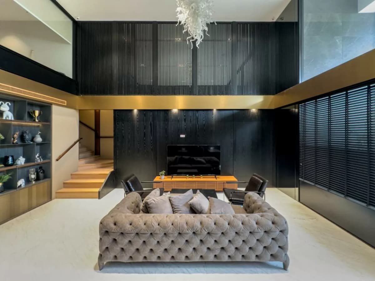 A high-angle shot of a modern lounge featuring a tufted grey sofa, marble floors, a black wood-paneled feature wall, and a gold-trimmed mezzanine.