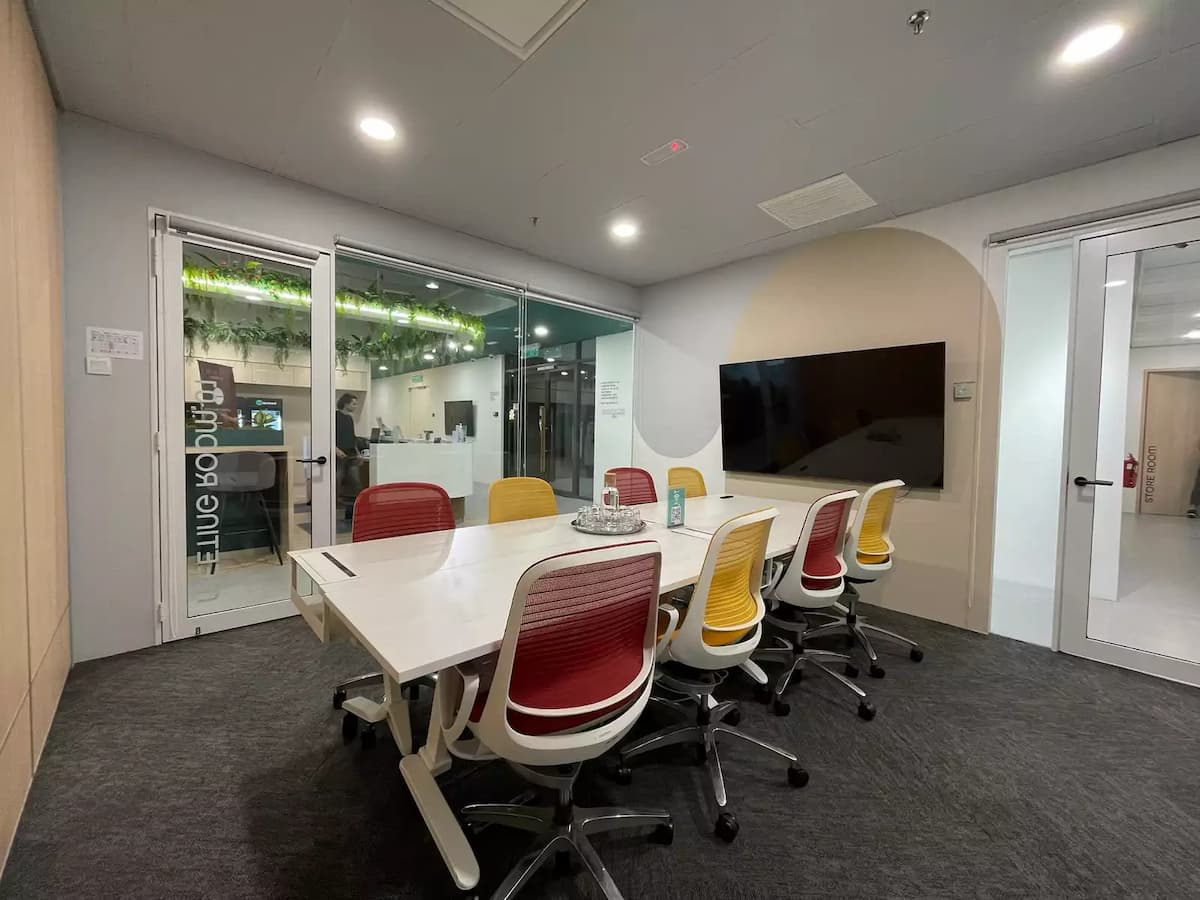 Modern meeting room with white conference table, red and yellow chairs, wooden wall panels, and glass partition