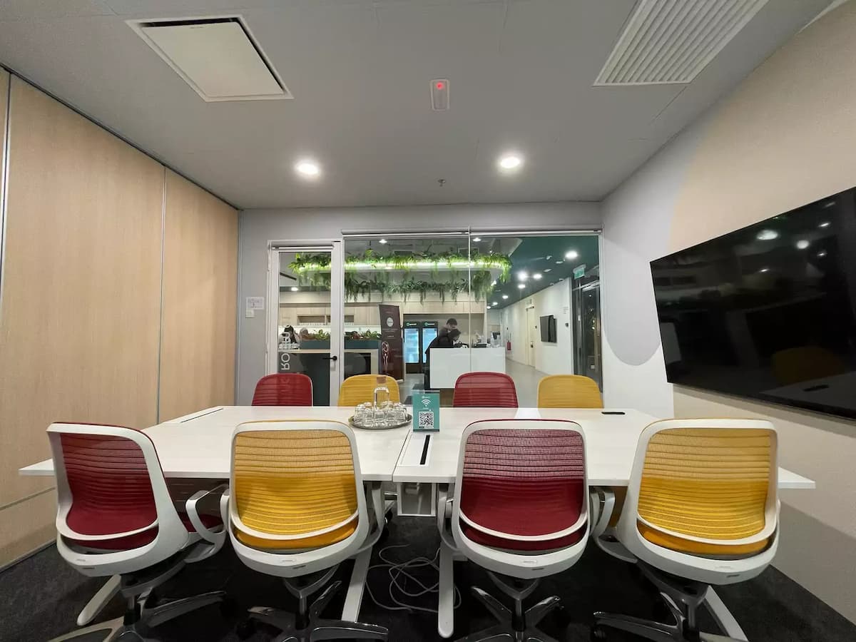 Modern meeting room with white conference table, red and yellow chairs, wooden wall panels, and glass partition