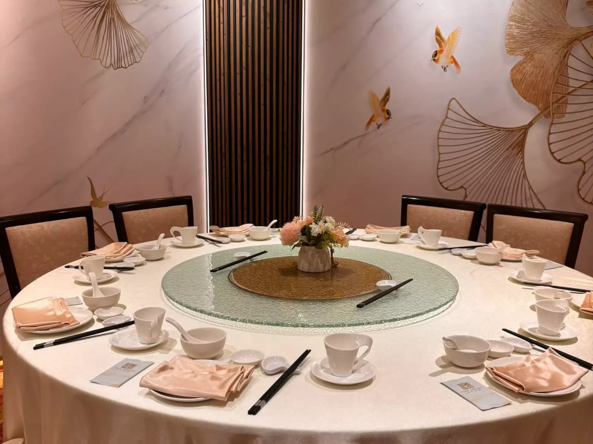 Round private dining table set with elegant place settings, floral centerpiece, and gold-accented wall art backdrop.