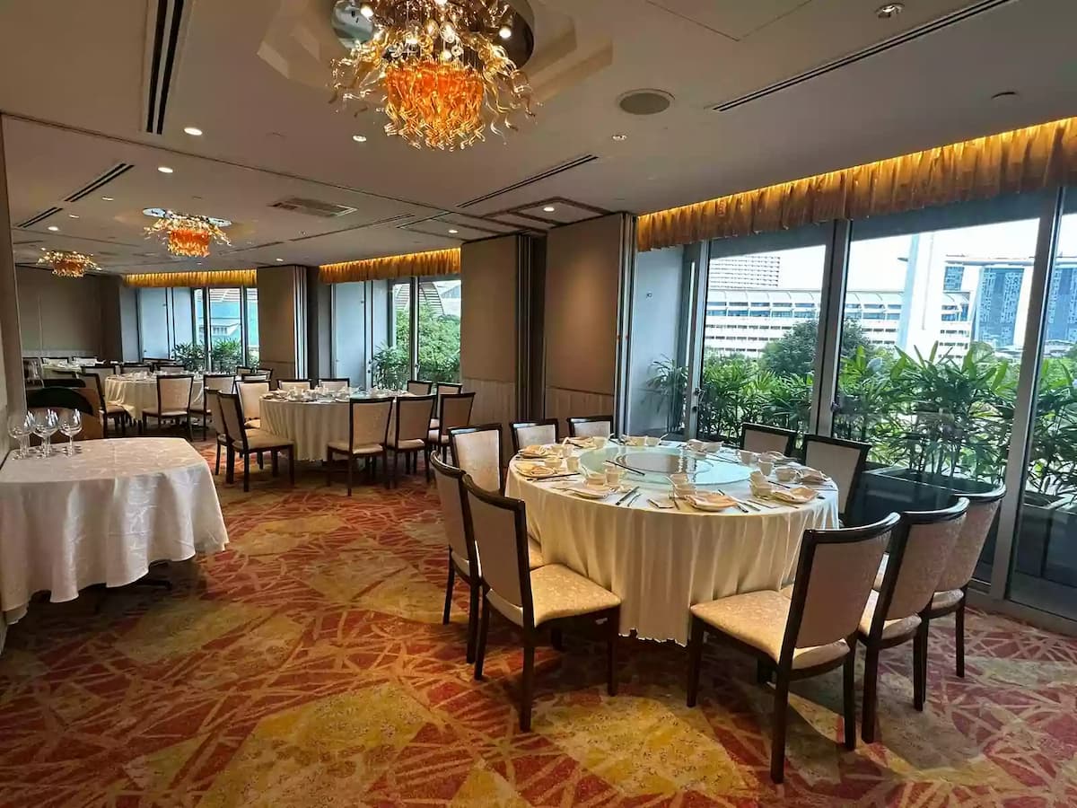 Elegant banquet dining hall with round tables, warm chandelier lighting, patterned carpet, and panoramic window views.