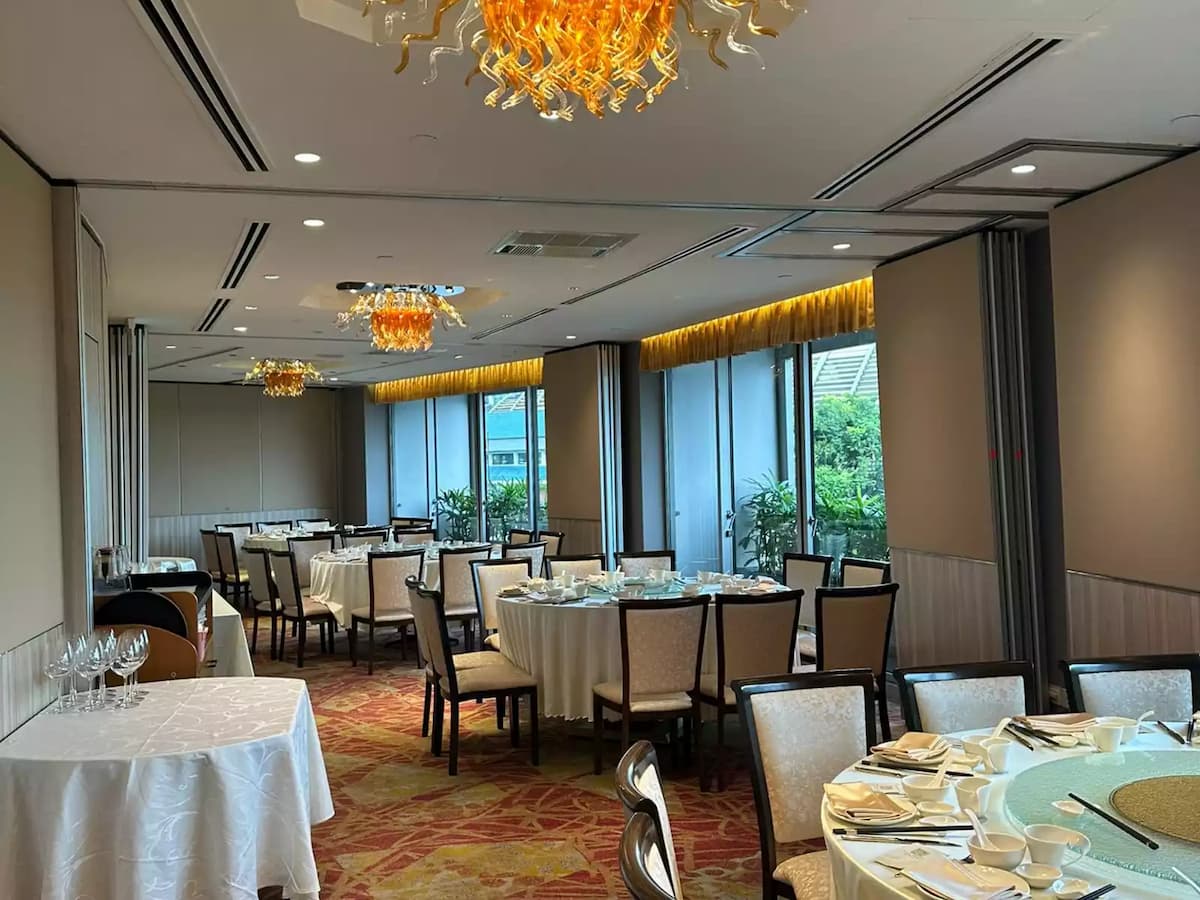 Elegant banquet room with round tables, crystal chandeliers, warm lighting, and window views of greenery.