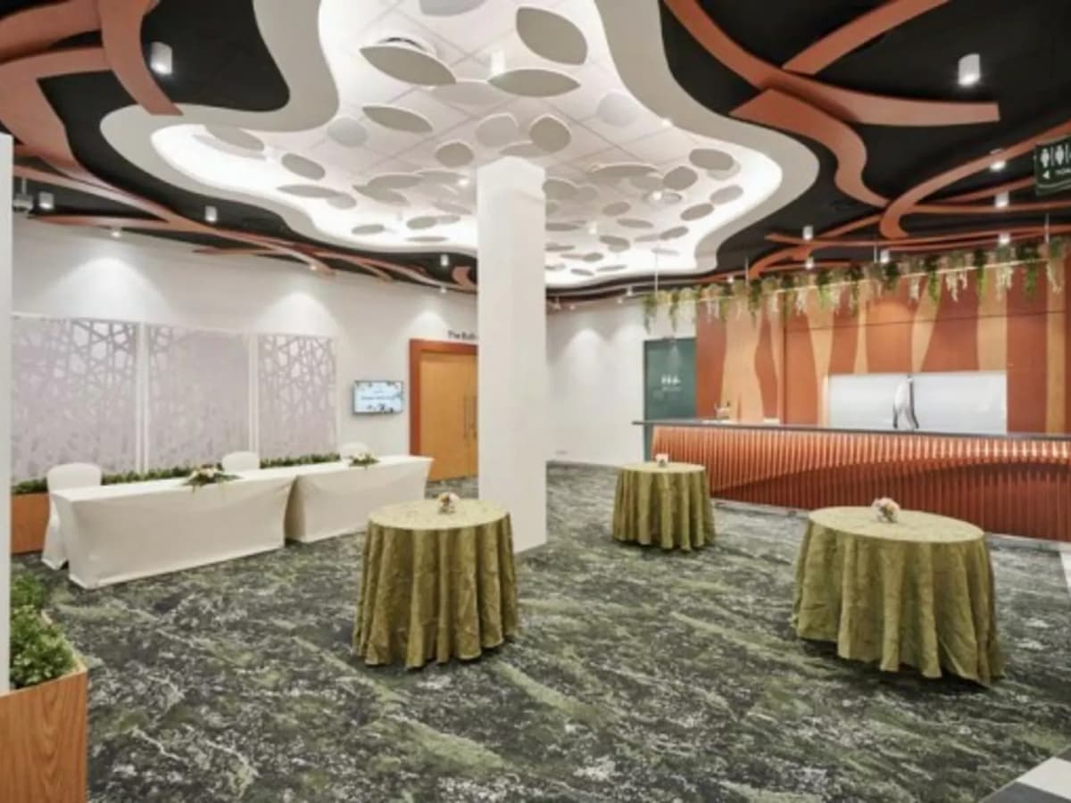 Modern event foyer with sculptural ceiling design, cocktail tables with green linens, buffet counters, and contemporary lighting.