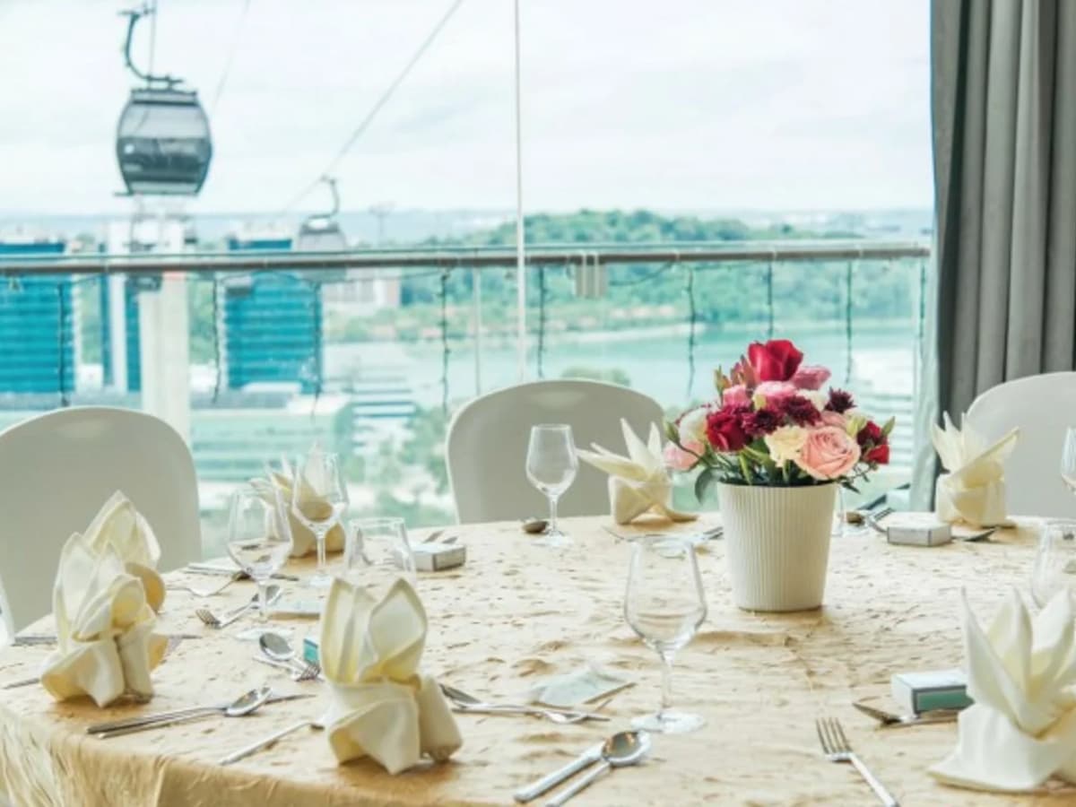 Elegant round dining table with folded napkins and floral centerpiece, set against floor-to-ceiling windows with cable car and city views.