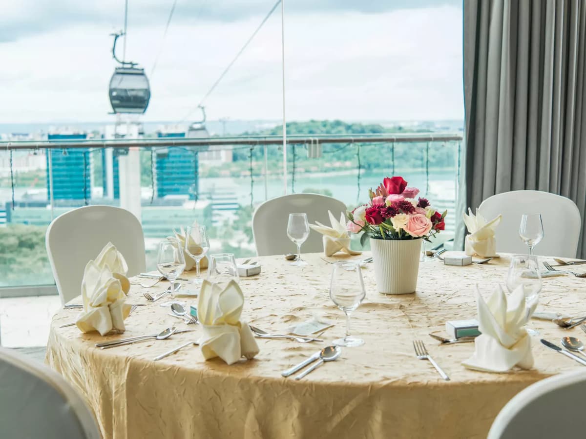 Elegant round dining table with folded napkins and floral centerpiece, set against floor-to-ceiling windows with cable car and city views.