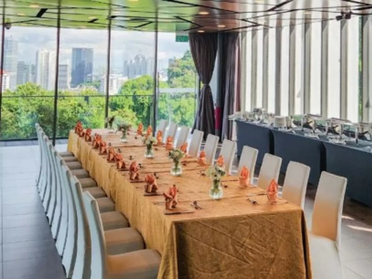 Long banquet table with gold tablecloth, orange folded napkins, and city skyline views through floor-to-ceiling windows