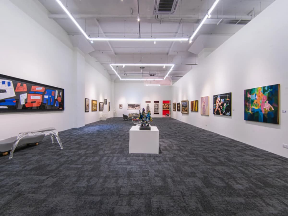 A wide exhibition room with dark grey carpet, a central sculpture on a pedestal