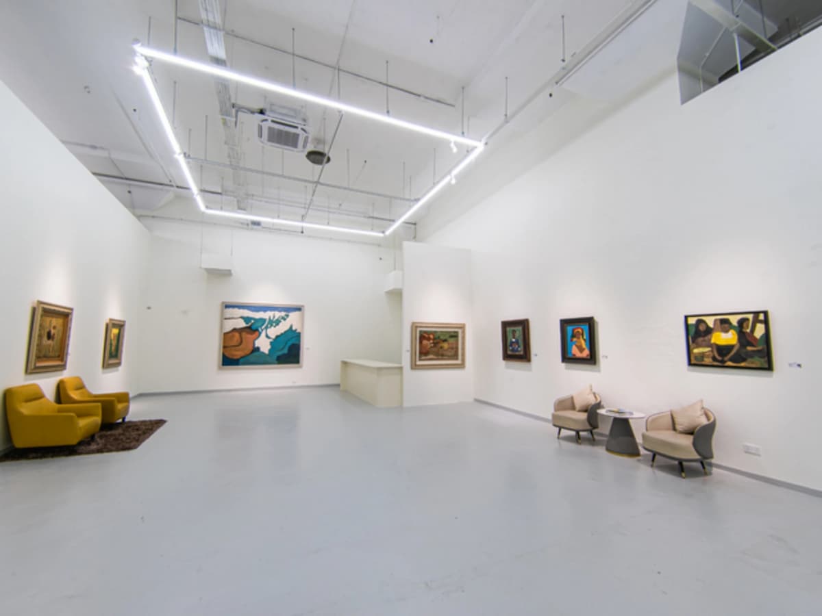A minimalist gallery space featuring yellow and beige armchairs on dark rugs