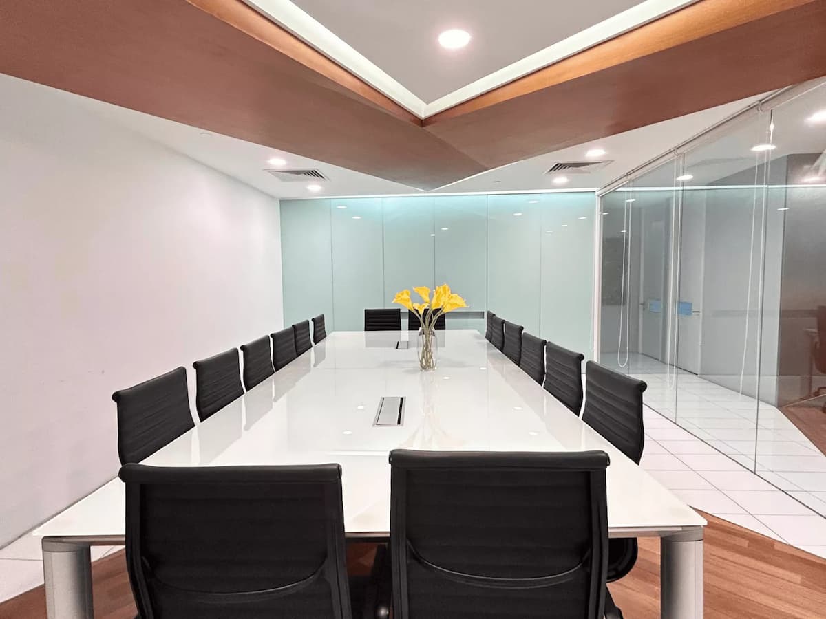 Modern boardroom with long white conference table, black swivel chairs, and glass partition walls.