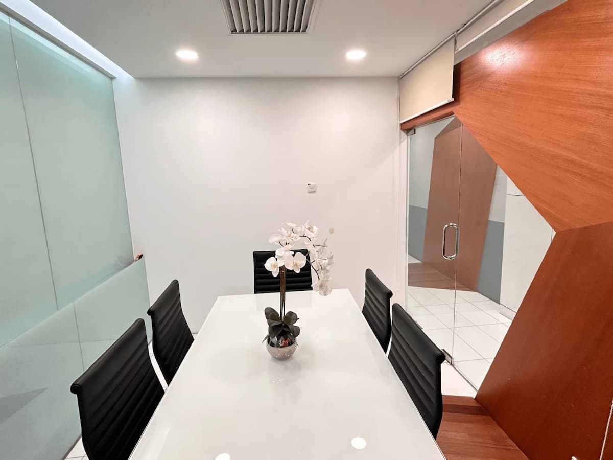 Compact meeting room with white table, black chairs, wood panel walls, and frosted glass partition.
