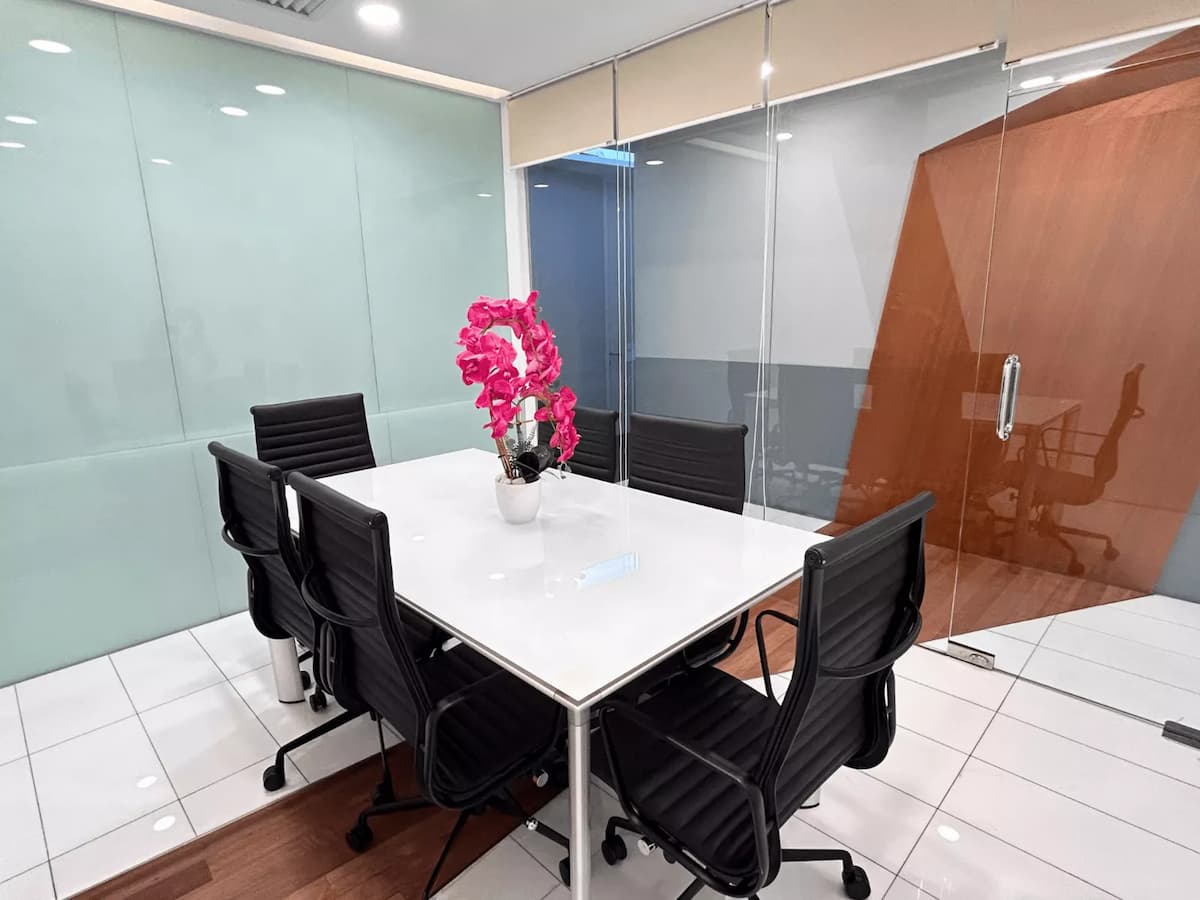 meeting room with white table, black chairs, glass walls, and pink orchid centerpiece.