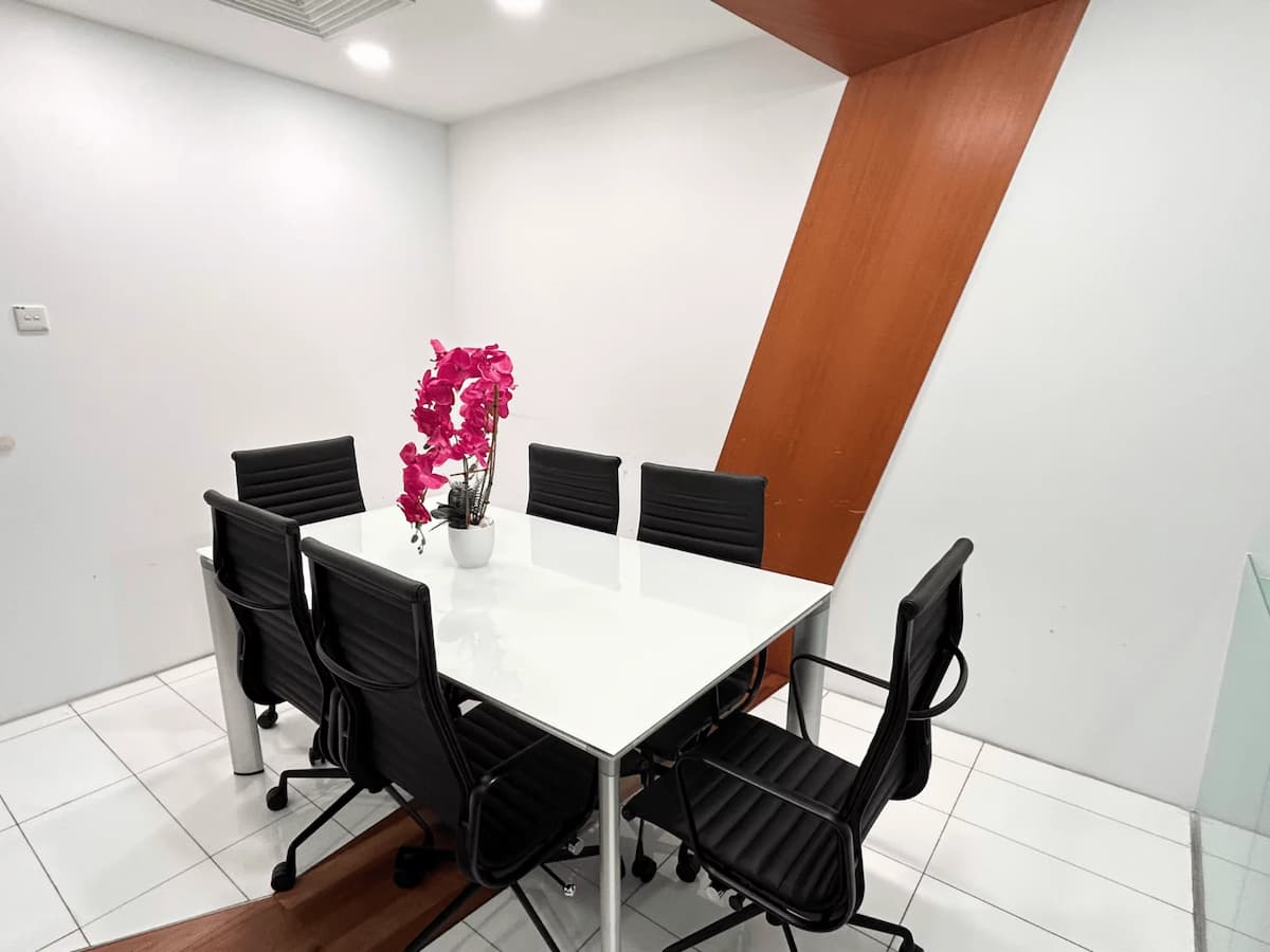 Minimalist meeting room with white table, black chairs, glass walls, and pink orchid centerpiece.