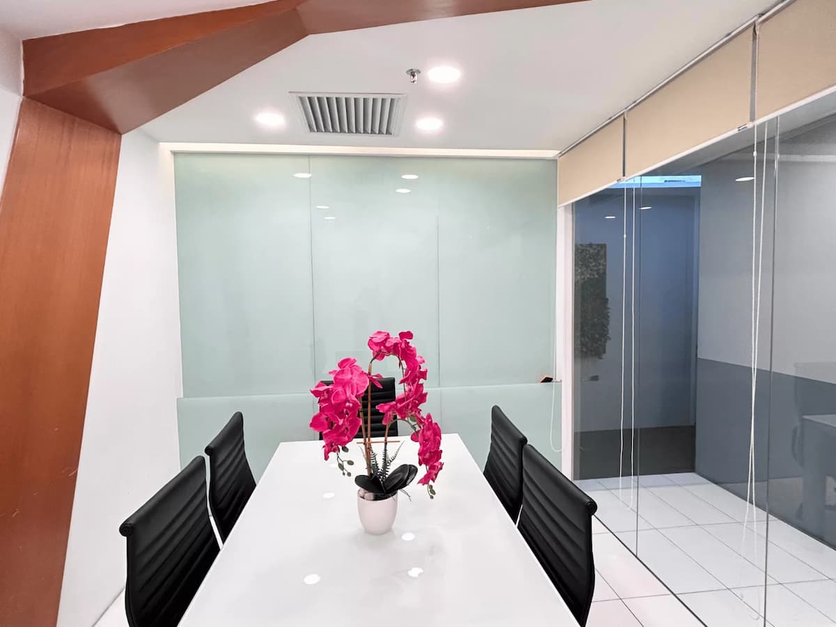 Meeting room with white table, black chairs, glass walls, and pink orchid centerpiece.