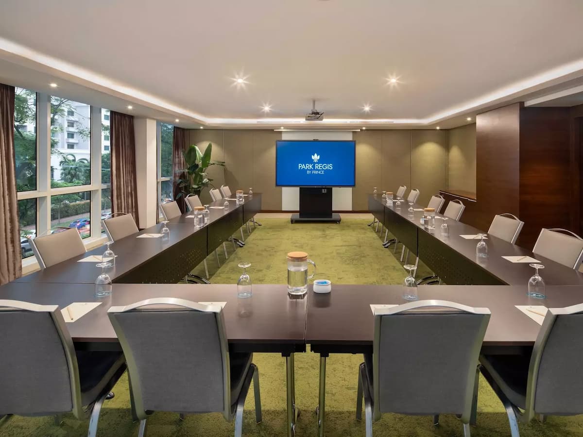 Boardroom meeting setup with U-shaped tables and presentation screen.