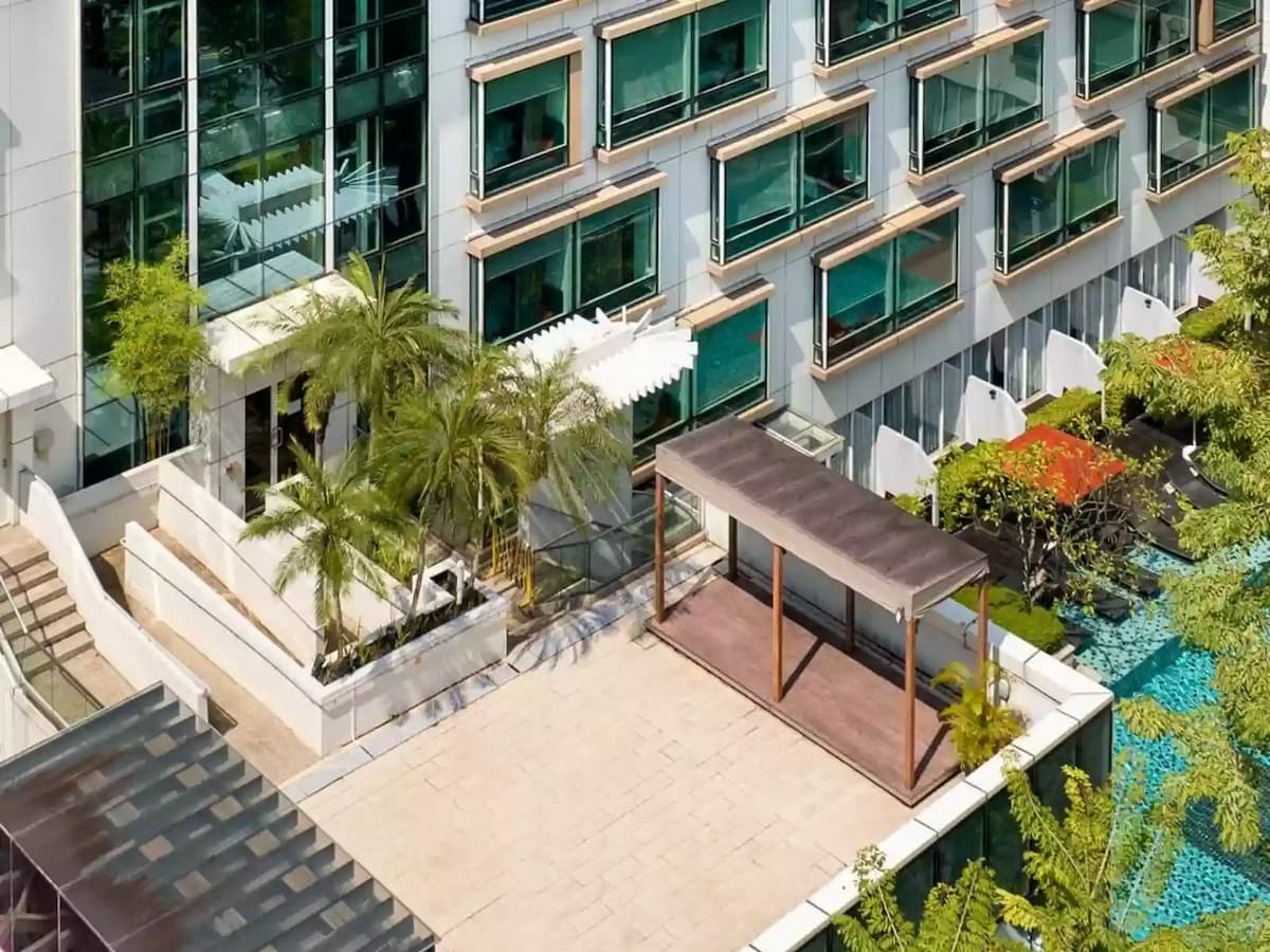 Hotel terrace overlooking pool area with greenery and shaded walkway.