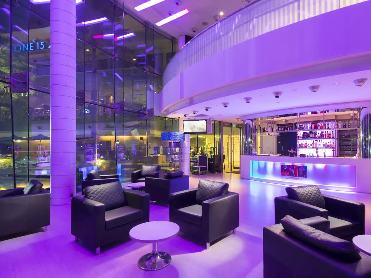 Stylish lounge event space with illuminated bar, modern seating, and purple ambient lighting.