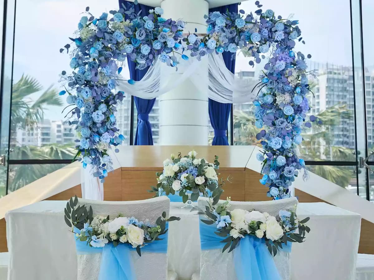 Blue floral wedding arch with white drapery and couple chairs.