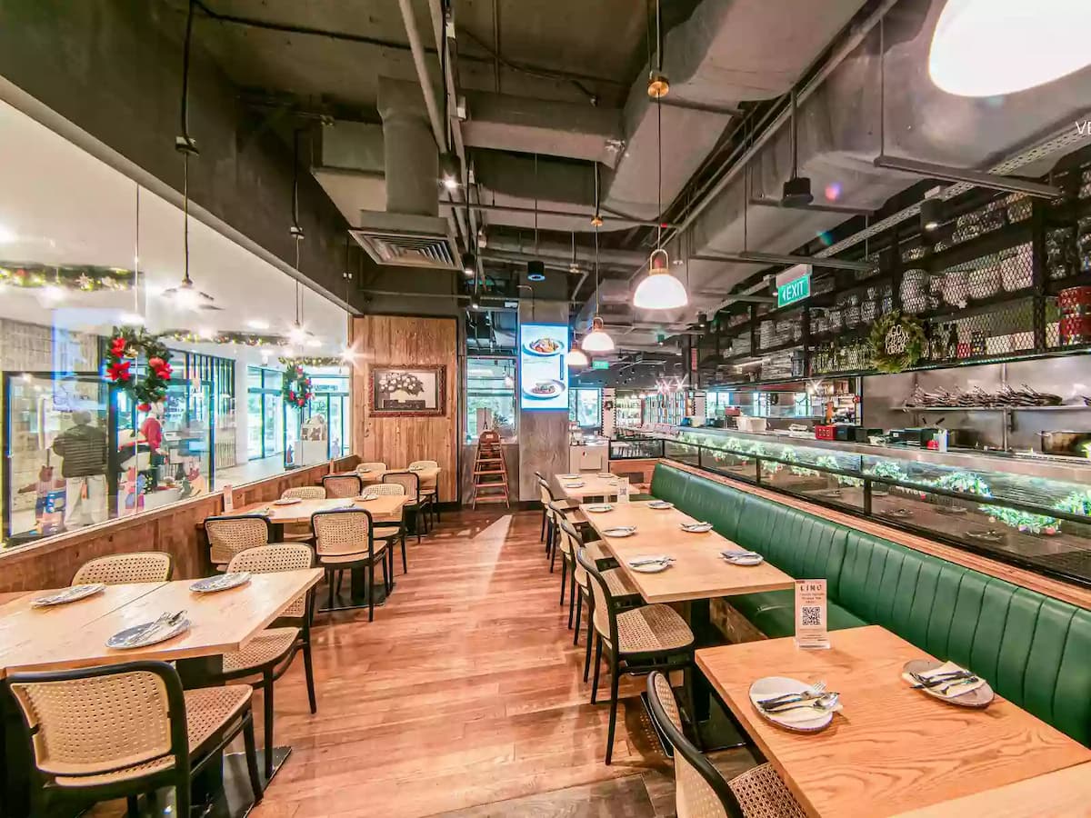 Modern Italian restaurant interior with green leather banquette seating, wooden tables, open kitchen counter, and warm pendant lighting.