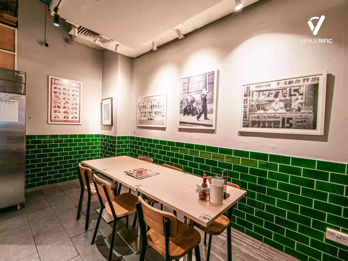 Cozy private dining room with a long wooden table, green tiled walls, framed vintage Italian photos, and simple wooden chairs