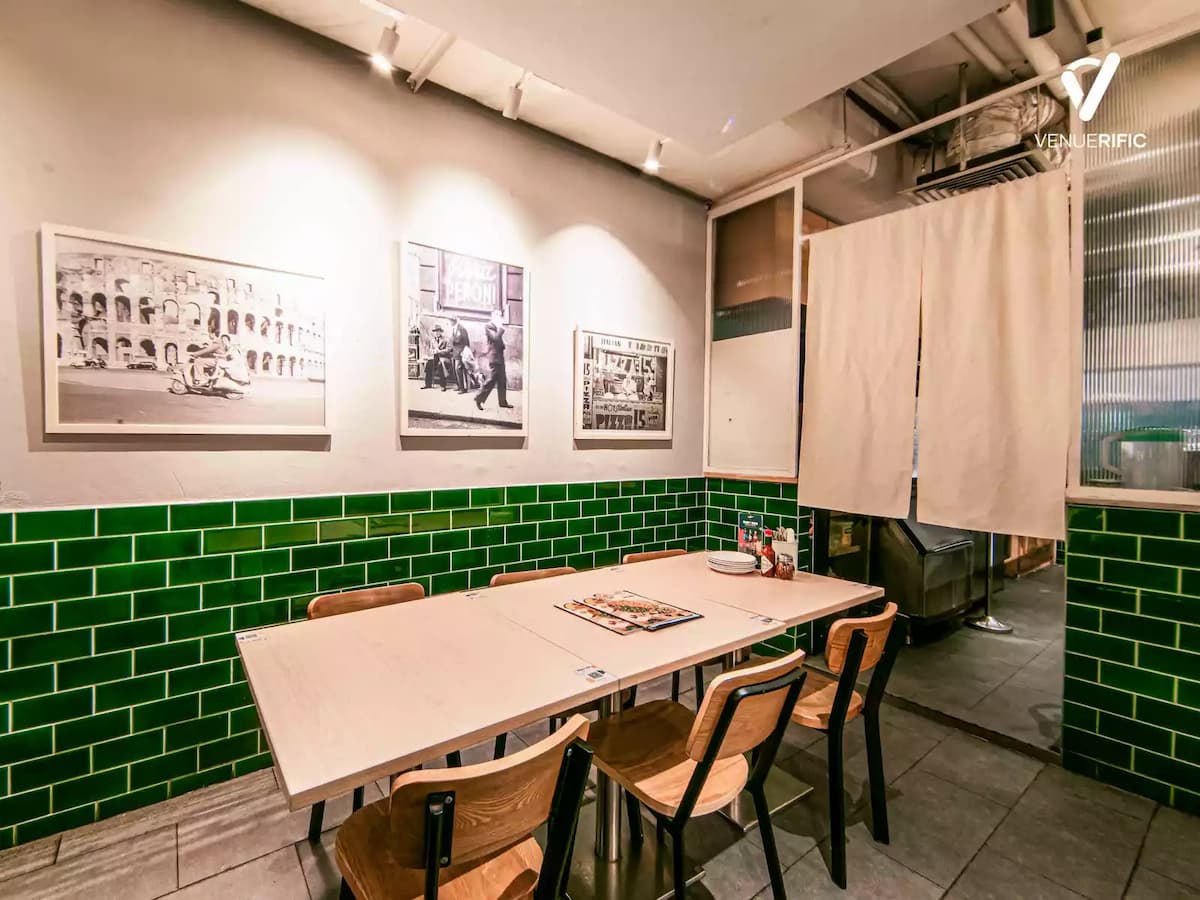 Private dining area with a light wood table, green tiled walls, framed black-and-white photos, and a curtain entrance in a cozy restaurant setting