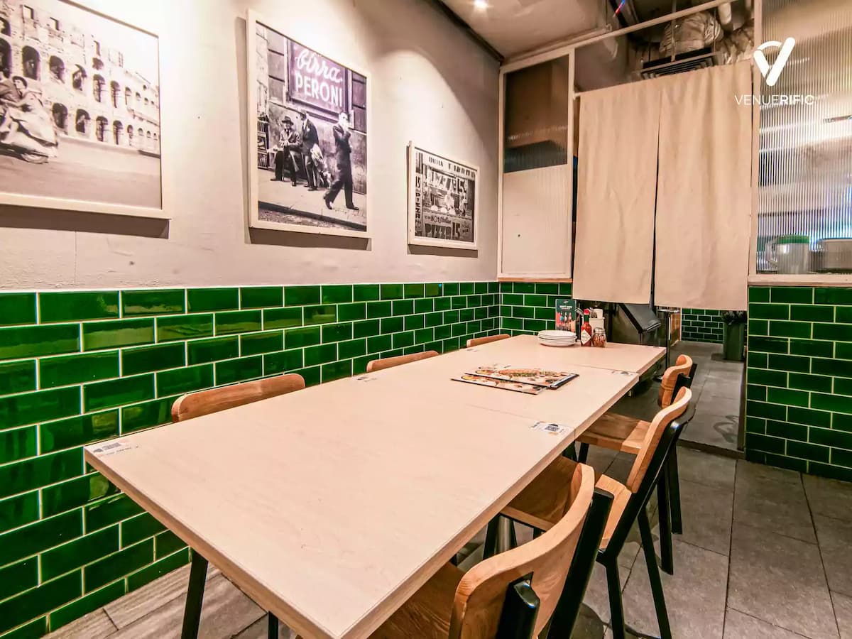 Private dining table with light wood finish, green tiled walls, framed vintage artwork, and minimalist seating in a cozy restaurant corner.