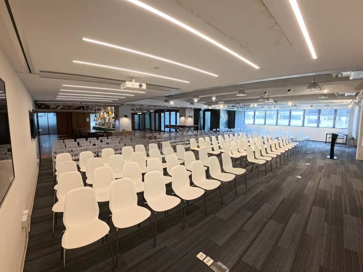 Conference-style event space with rows of white chairs, projector setup, and modern industrial ceiling lighting.