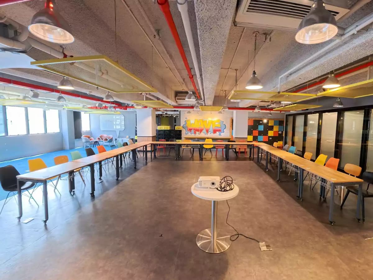 Modern meeting space with U-shaped wooden tables, colorful chairs, graffiti wall art, and glass meeting rooms.