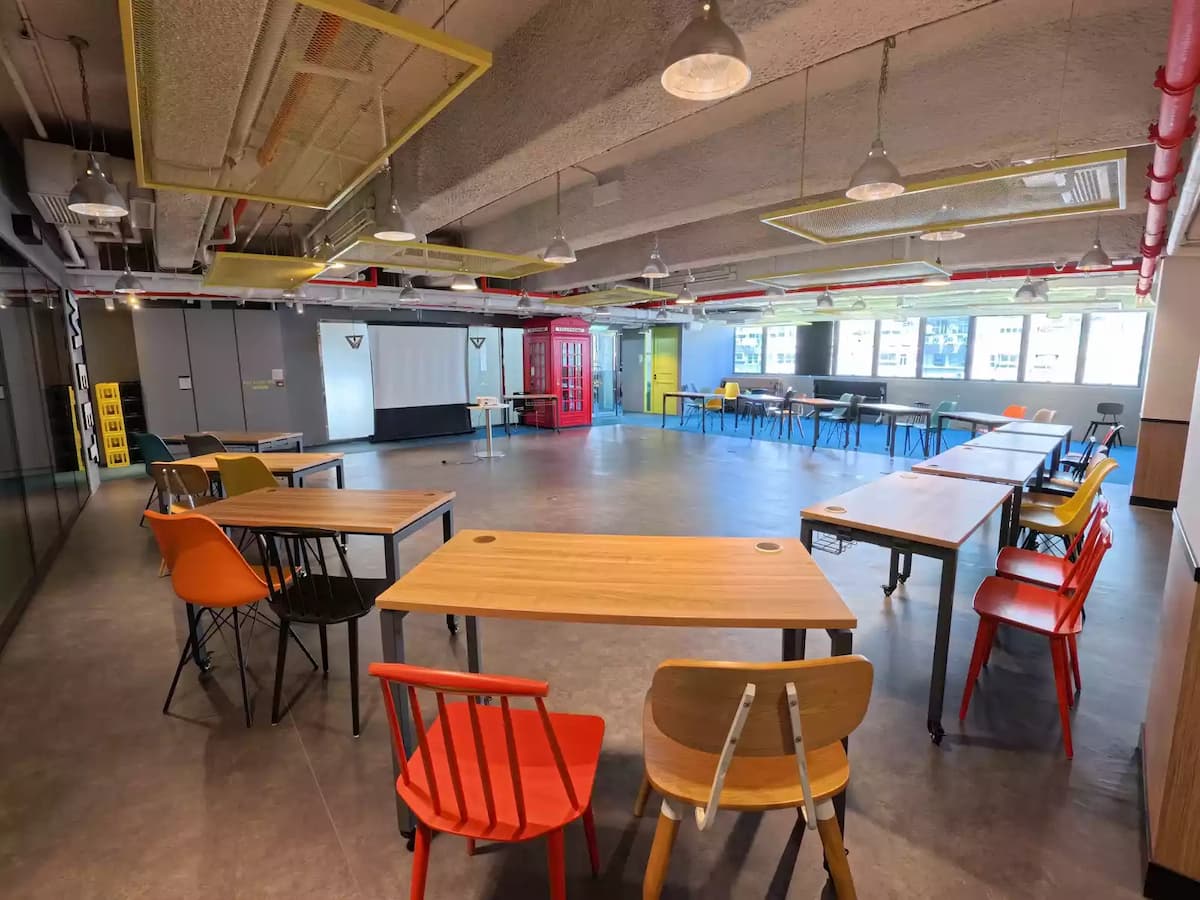 Flexible workshop space with wooden tables, colorful chairs, projector screen, and bright industrial-style ceiling.