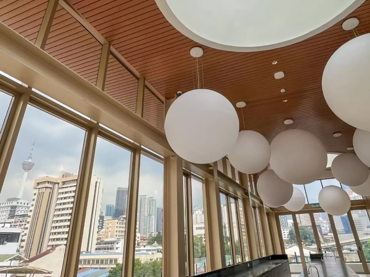 Ceiling detail with globe pendant lights, warm wood panels, and floor-to-ceiling windows overlooking the city skyline.