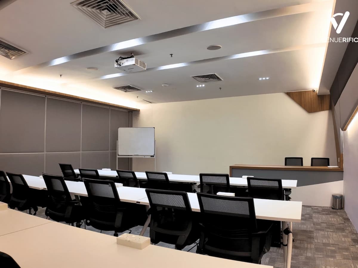 Mutiara Event Space in classroom-style layout with long tables, presentation desk, whiteboard, and ceiling-mounted projector