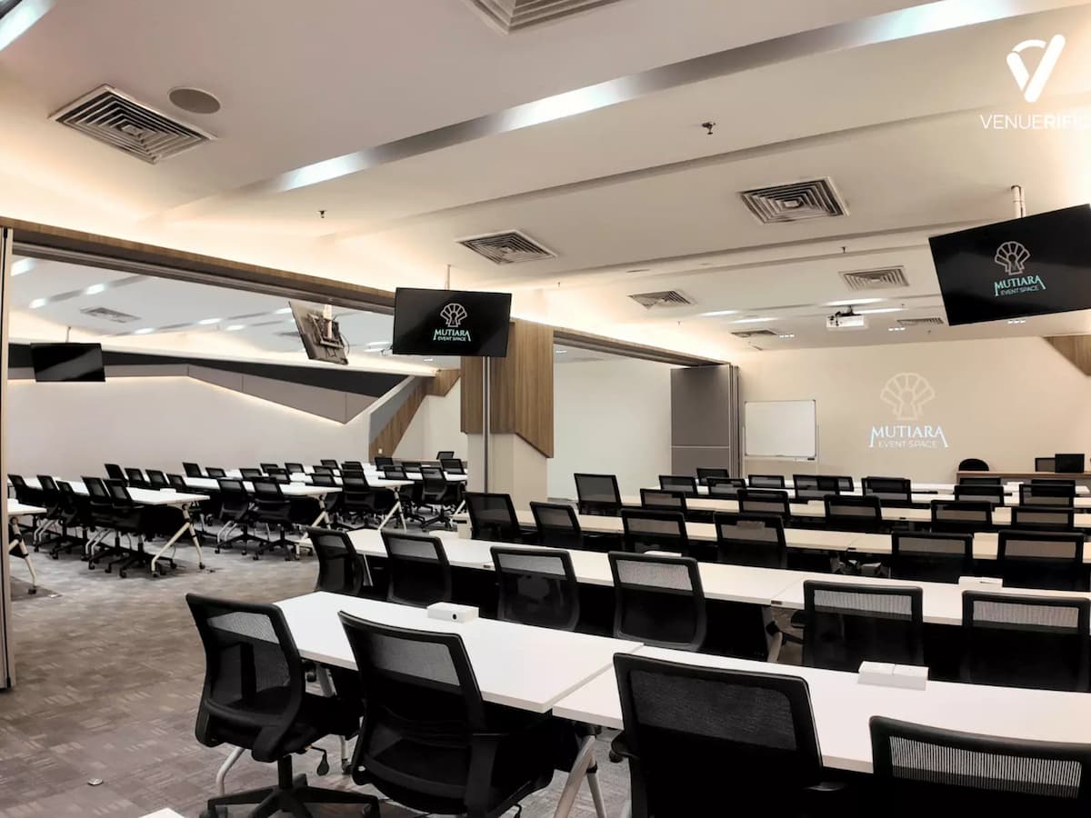 Mutiara Event Space set up in a large classroom-style layout with long tables, ergonomic chairs, and multiple presentation screens