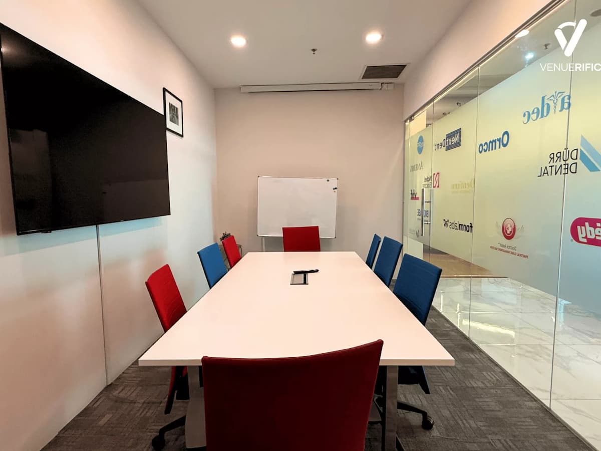 Small meeting room at Mutiara Event Space with boardroom table, colourful chairs, whiteboard, and wall-mounted TV