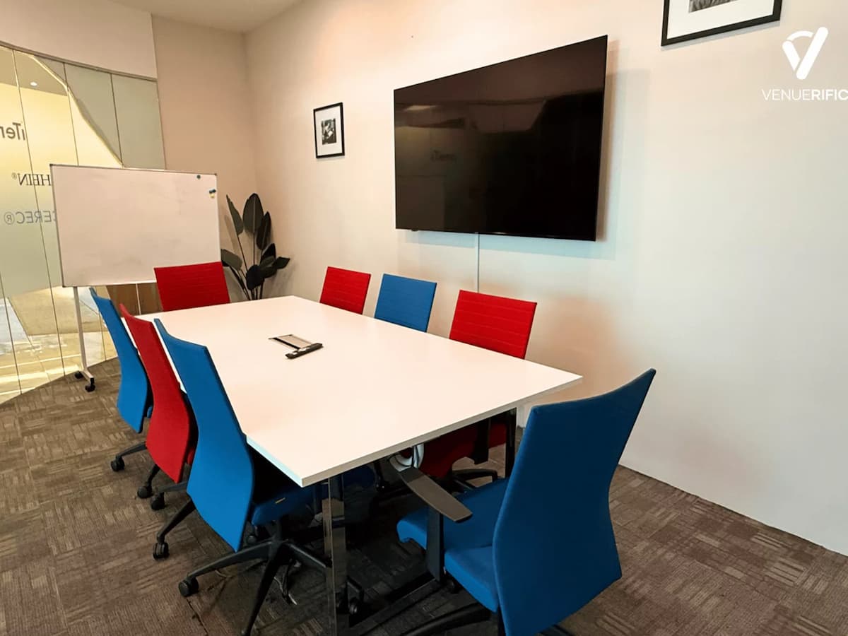 Private meeting room at Mutiara Event Space with boardroom table, colourful chairs, whiteboard, and wall-mounted TV