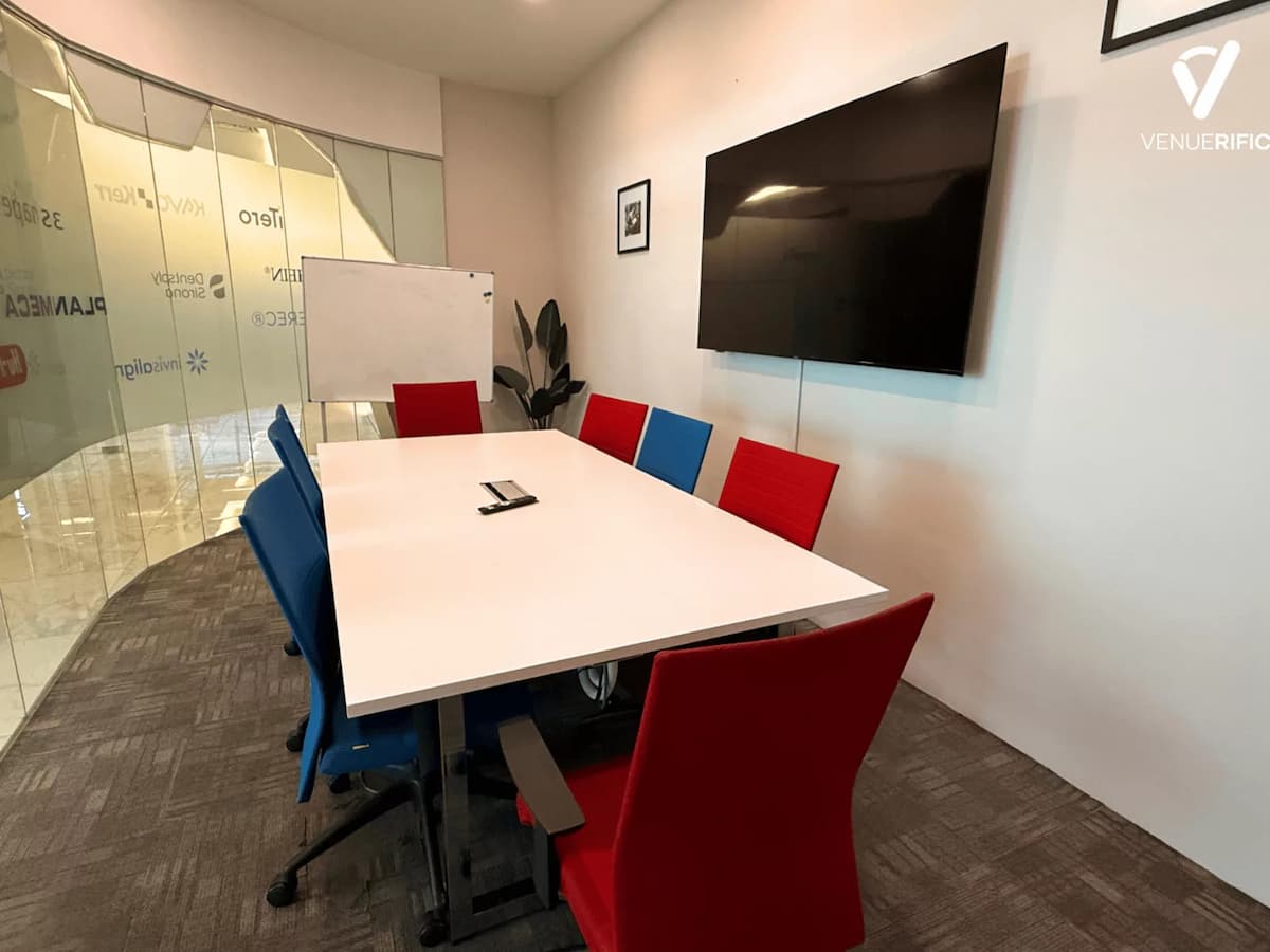 Private meeting room at Mutiara Event Space with boardroom table, colourful chairs, whiteboard, and wall-mounted TV for discussions