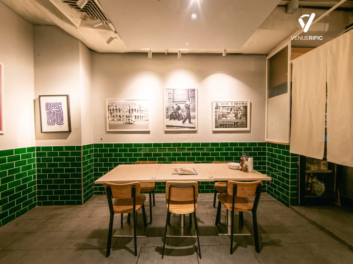 Cozy private dining corner with wooden table seating, green tiled walls, and framed black-and-white artwork under warm lighting.