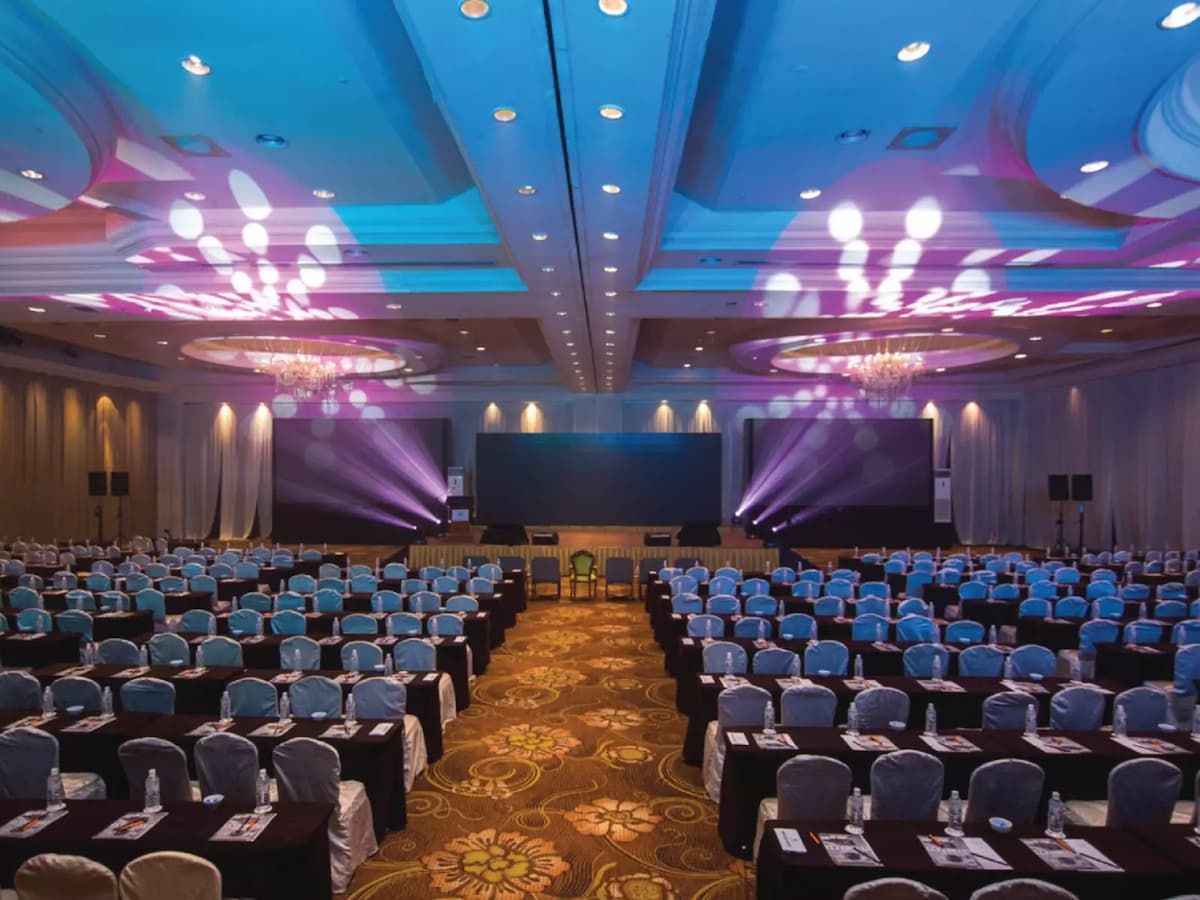 Grand conference ballroom with theatre-style seating, stage lighting, and a central presentation area—perfect for large corporate conferences, seminars, product launches, and business conventions.