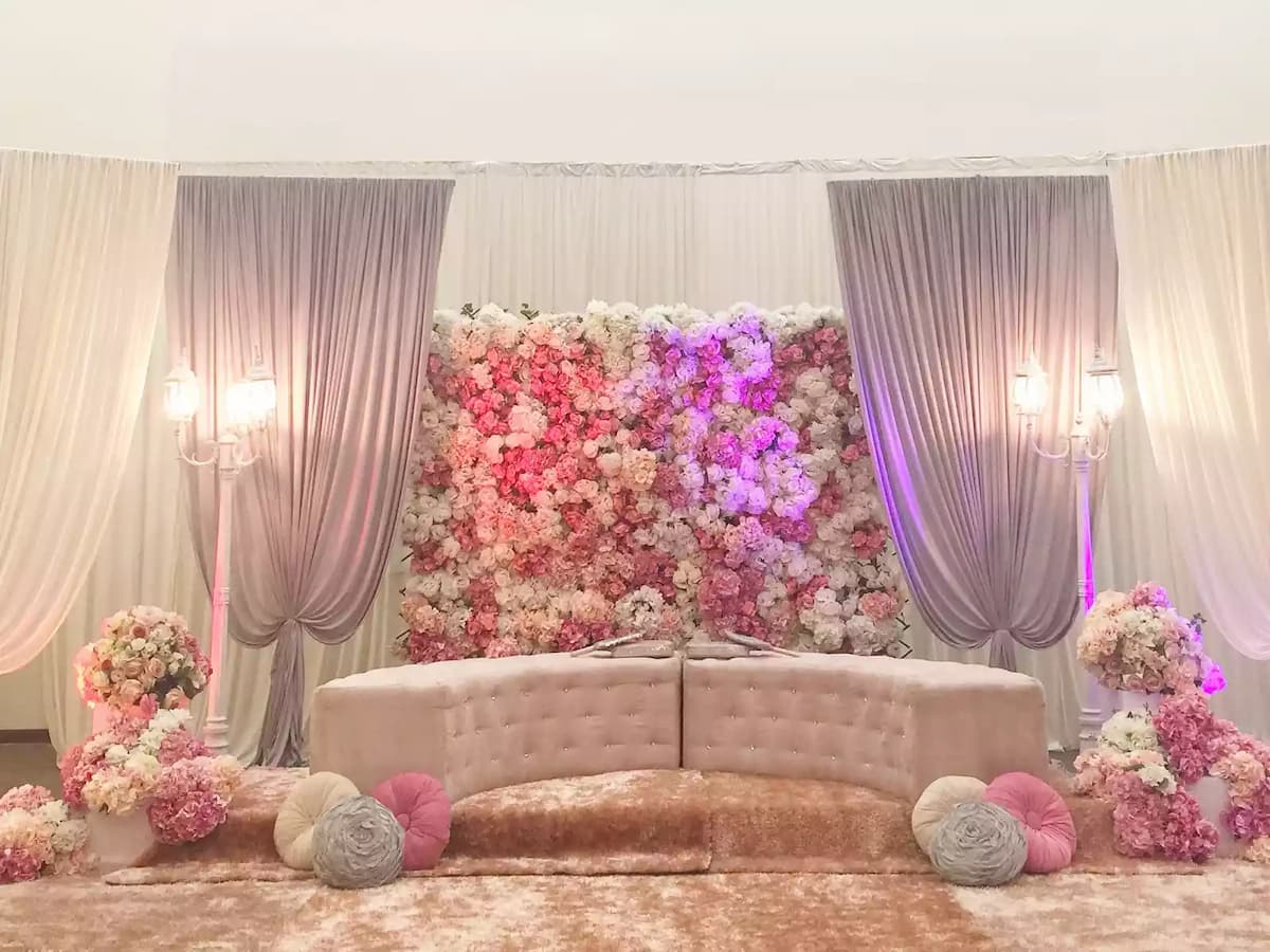 Elegant wedding or engagement stage featuring a floral backdrop, draped curtains, and a plush seating sofa—ideal for solemnizations, bridal receptions, and intimate celebration events.