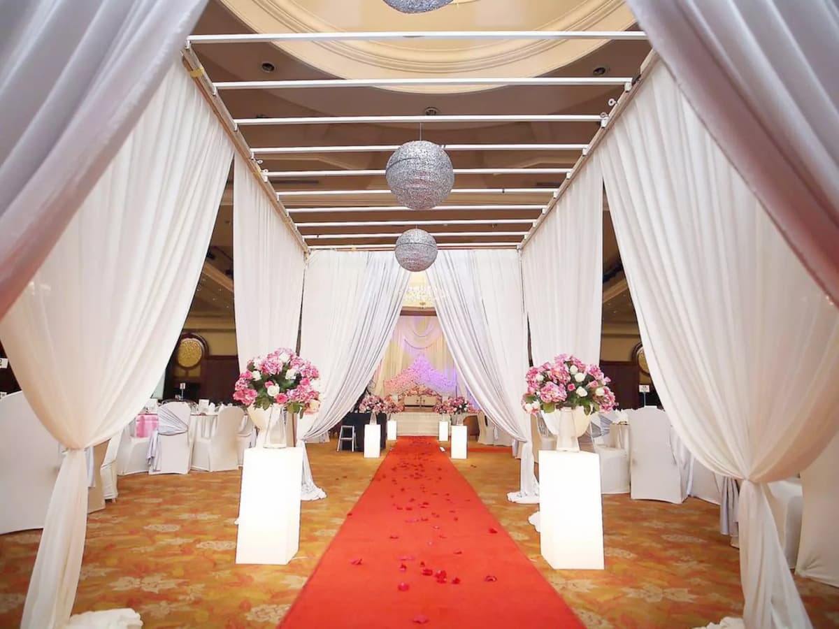 Elegant wedding aisle setup with draped white canopies, floral arrangements, and a red carpet walkway—perfect for solemnizations, wedding ceremonies, and romantic celebration events.