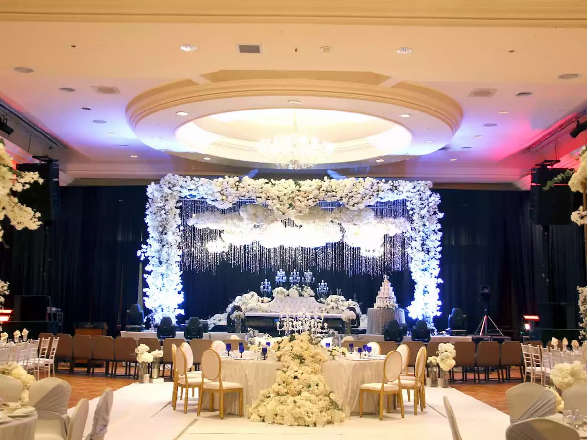 Grand ballroom wedding setup featuring a lavish floral stage backdrop, chandelier lighting, and round banquet seating—ideal for weddings, receptions, and elegant gala celebrations.