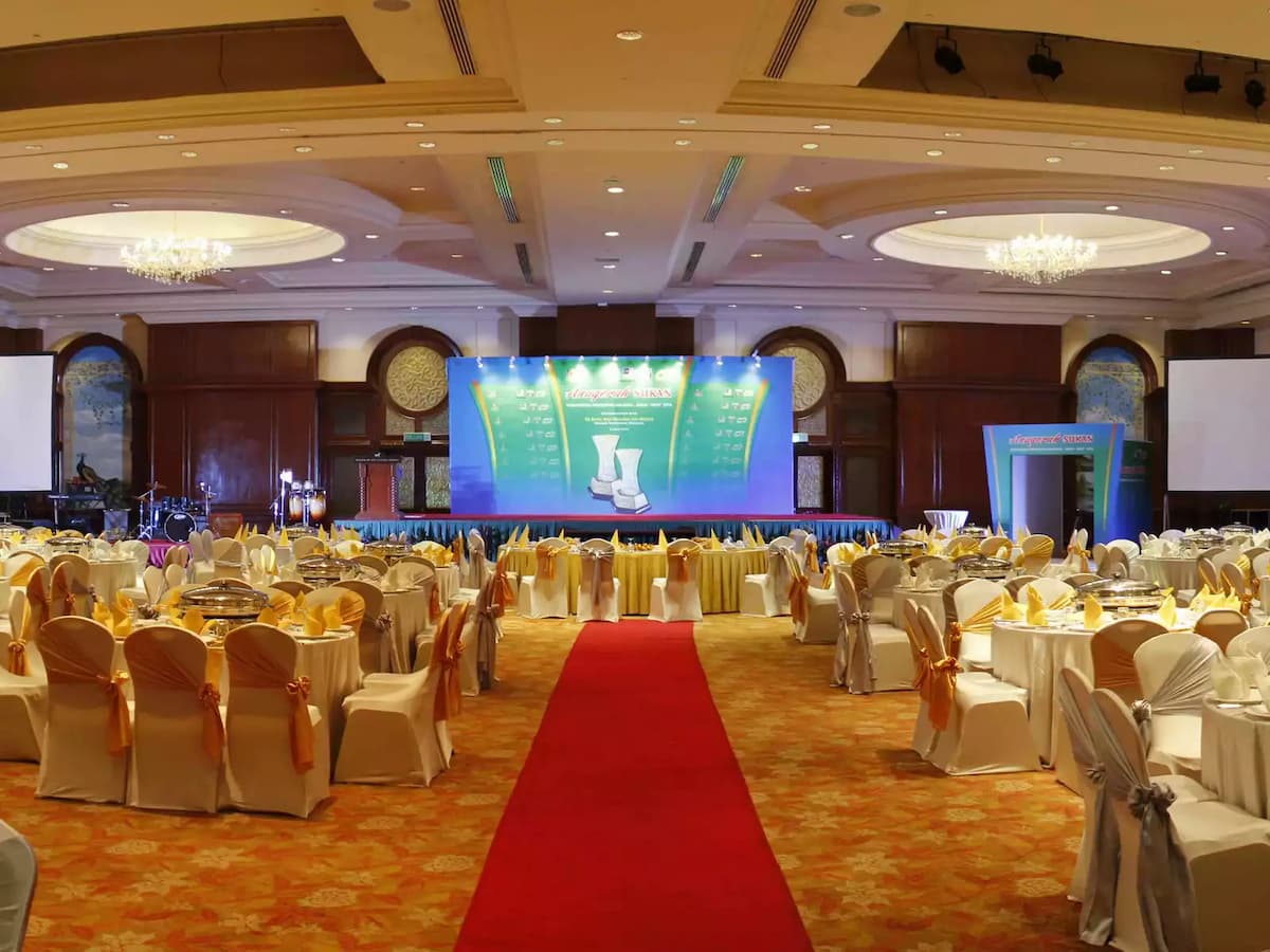 Spacious ballroom banquet setup with a central red carpet aisle, round dining tables, and a presentation stage—ideal for corporate dinners, award ceremonies, gala nights, and large formal events.