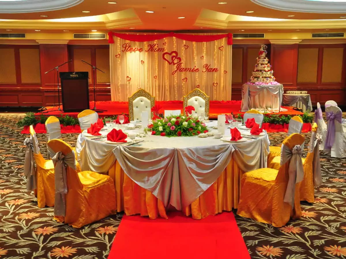 Wedding banquet setup with a decorated couple’s table, floral arrangements, and a red-carpet stage backdrop—perfect for wedding receptions, engagement celebrations, and formal banquet events.