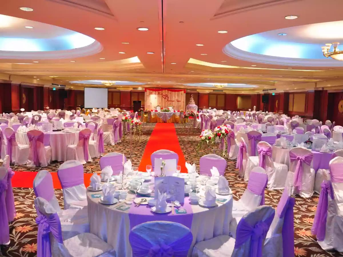 Grand ballroom wedding reception setup with round banquet tables, purple chair sashes, and a red carpet aisle leading to the stage—perfect for large weddings, receptions, and formal celebration events.
