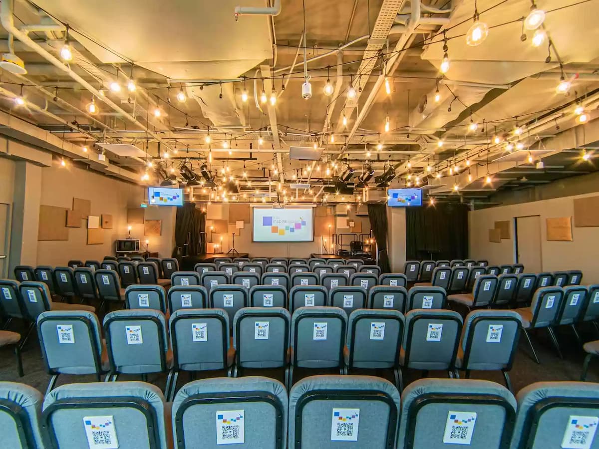 Modern event space with theatre-style seating, warm string lighting, and presentation screens—ideal for conferences, seminars, workshops, talks, and corporate training sessions.