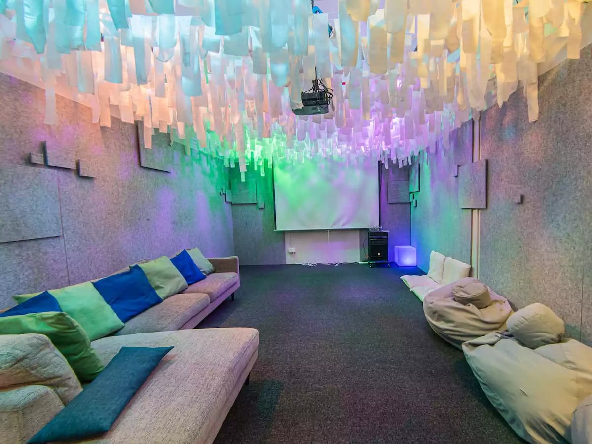 Creative immersive lounge space with hanging fabric ceiling installations, soft seating, bean bags, and a projector screen—ideal for workshops, film screenings, brainstorming sessions, team retreats, or interactive presentations.